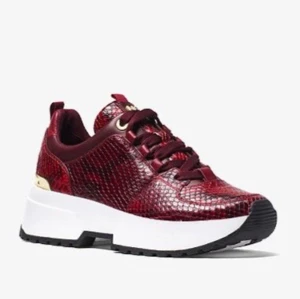 Michaelkors sneakers strl. 36 - Sneakers i vinröd snakeskinn från Michael kors. Guldiga detaljer. Använda men i fint skick, nyputsade. Något slitage på gulddetaljerna se bild 