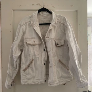 Vit jeansjacka från Warrick - Säljer en vintage vit jeansjacka från Warrick, tillverkad i Finland. Jackan har en klassisk design med knappar framtill och flera fickor. Den har en cool patch på ryggen med ett unikt mönster. Perfekt för vår och sommar!