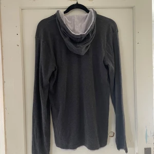 Grå hoodie i slim fit - Säljer en stilren grå hoodie i slim fit. Den har en mjuk och bekväm känsla med vita dragsnören i huvan. Perfekt för en avslappnad look under höst och vinter. Passar bra till både jeans och joggers!