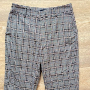 Rutig byxa från Gina Tricot - Säljer ett par snygga rutiga kostymbyxor från Gina Tricot. De är grå med ett klassiskt rutmönster. Byxorna har en dragkedja och knapp framtill, och de är perfekta för både vardag och fest. Passar bra till en stilren look!