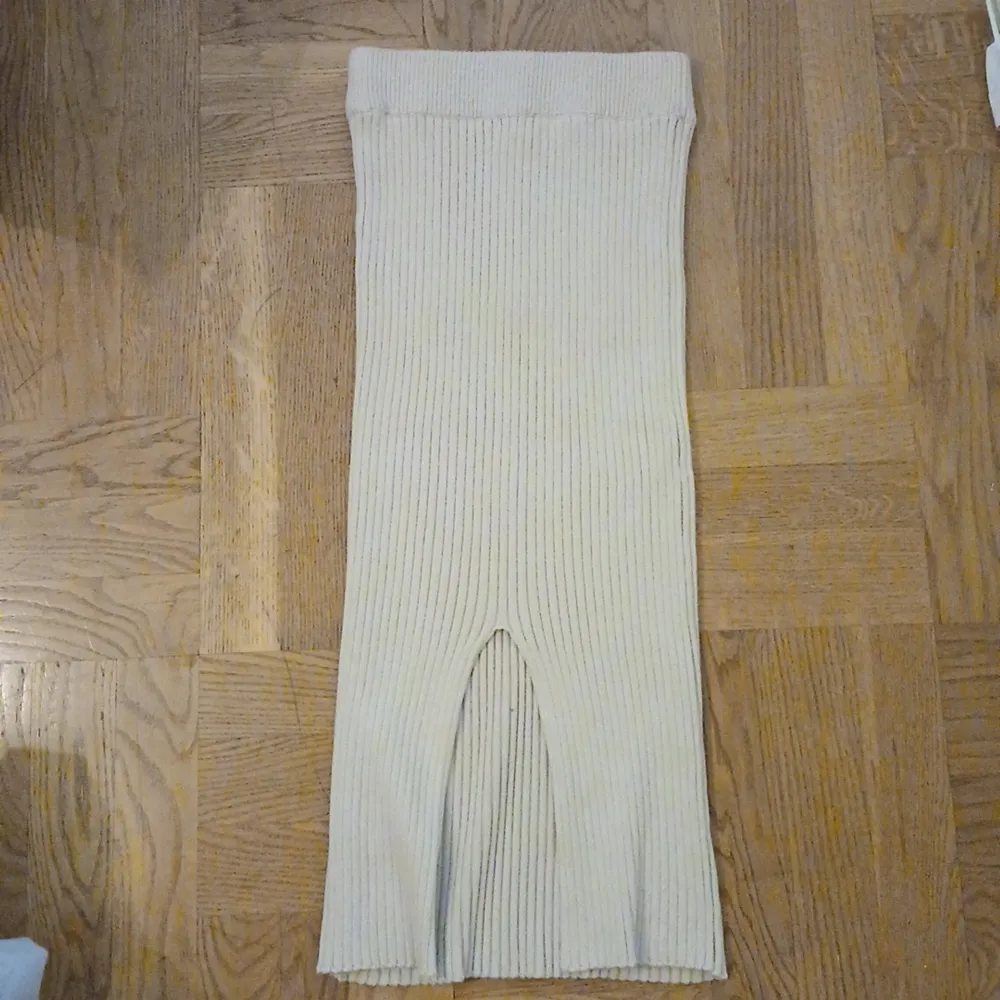 Säljer en superfin beige ribbad kjol som är perfekt för både vardag och fest. Kjolen har en slits framtill som ger den en snygg detalj och är gjord i ett mjukt och stretchigt material. Den är både bekväm och stilren, vilket gör den lätt att matcha med olika toppar och skor.. Kjolar.