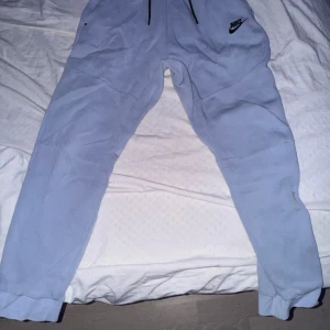 Ljusblå mjukisbyxor från Nike - Säljer ett par ljusblå mjukisbyxor från Nike för passar inte mig längre. behöver tvättas annars är dom fina. De är superbekväma och perfekta för chill dagar eller träning. Byxorna har en elastisk midja med dragsko och muddar vid bensluten. Det finns också fickor med dragkedja för säker förvaring av småsaker. Nike-loggan är snyggt placerad på ena benet.
