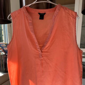 Korallfärgad ärmlös topp från Lindon - Säljer en snygg korallfärgad ärmlös topp från Lindon. Den har en v-ringad design och är perfekt för sommardagar. Materialet känns lätt och luftigt, vilket gör den idealisk för varma väder. Passar både till vardags och festligare tillfällen!