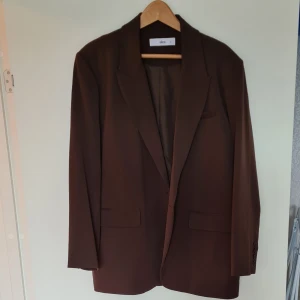 Kvavaj från Ellos  - Mörkbrun blazer i storlek 42 Rak modell Fickor fram  Slits nedtill bak Längd 74cm i stl 36  Använd fåtal gånger, nästan som ny. Lite oversized modell Kan bli ett set med byxorna från ellos här bredvid 