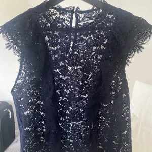 Svart spetsblus från Zara - Säljer en elegant svart spetsblus från Zara. Den är ärmlös och har ett vackert spetsmönster som ger en lyxig känsla. Perfekt för festliga tillfällen eller en utekväll. Blusen är i storlek L och är tillverkad i Marocko.