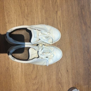 Vita sneakers i skinn - Säljer ett par vita sneakers i skinn. De har en klassisk design med snörning och en tjock sula. Skorna är välanvända med synligt slitage, speciellt vid hälen där materialet har börjat flagna. Perfekta för vardagsbruk om du gillar en avslappnad stil. Dom är väldigt sköna och passar både tjej o kille💕