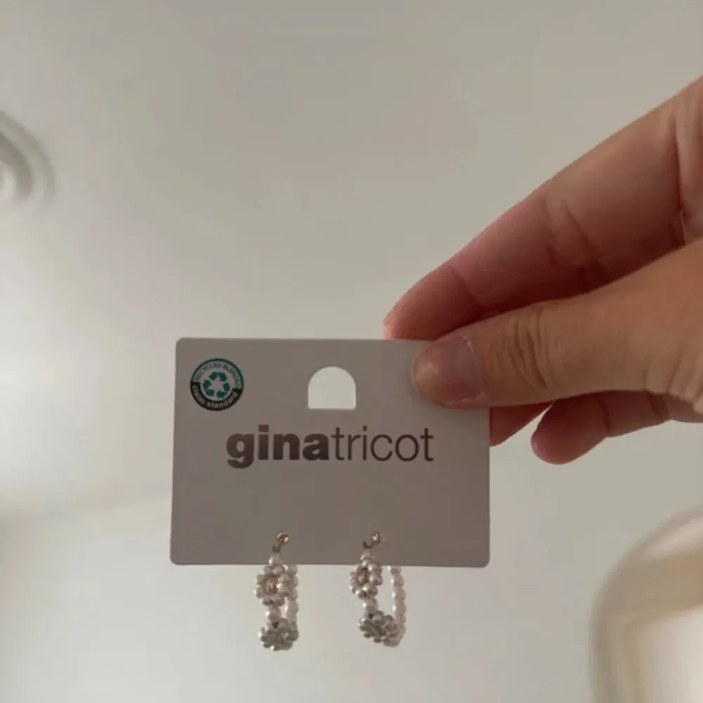 Två par örhängen från Gina Tricot. Det ena paret är små creoler med vita pärlor, perfekt för en elegant look. Det andra paret är guldfärgade creoler med färgglada stenar, idealiska för att lägga till lite färg till din outfit.. Asusteet.