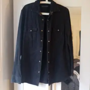 Säljer en snygg svart overshirt som är perfekt för lager-på-lager-stilen. Den har långa ärmar och knappar framtill, vilket ger en cool och avslappnad look. Passar perfekt till både vardag och fest!