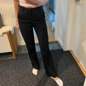 Svarta kostymbyxor - Säljer ett par stilrena svarta kostymbyxor. De och har en rak passform som ger en klassisk look. Perfekta för både kontoret och mer formella tillfällen. Byxorna är i nyskick och har en snygg dragkedja och knapp framtill.