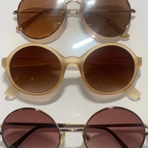 Tre par solglasögon i olika stilar - Säljer tre par solglasögon i olika stilar. Första paret har en klassisk aviator-stil med bruna linser och guldfärgad metallram. Andra paret är runda med en beige plastbåge och bruna linser. Tredje paret har en retro look med runda rosa linser och guldfärgad metallram. Perfekta för sommardagar och festivaler! 1 par för 50, 2 för 75 & alla 3 för 120kr! ☺️   