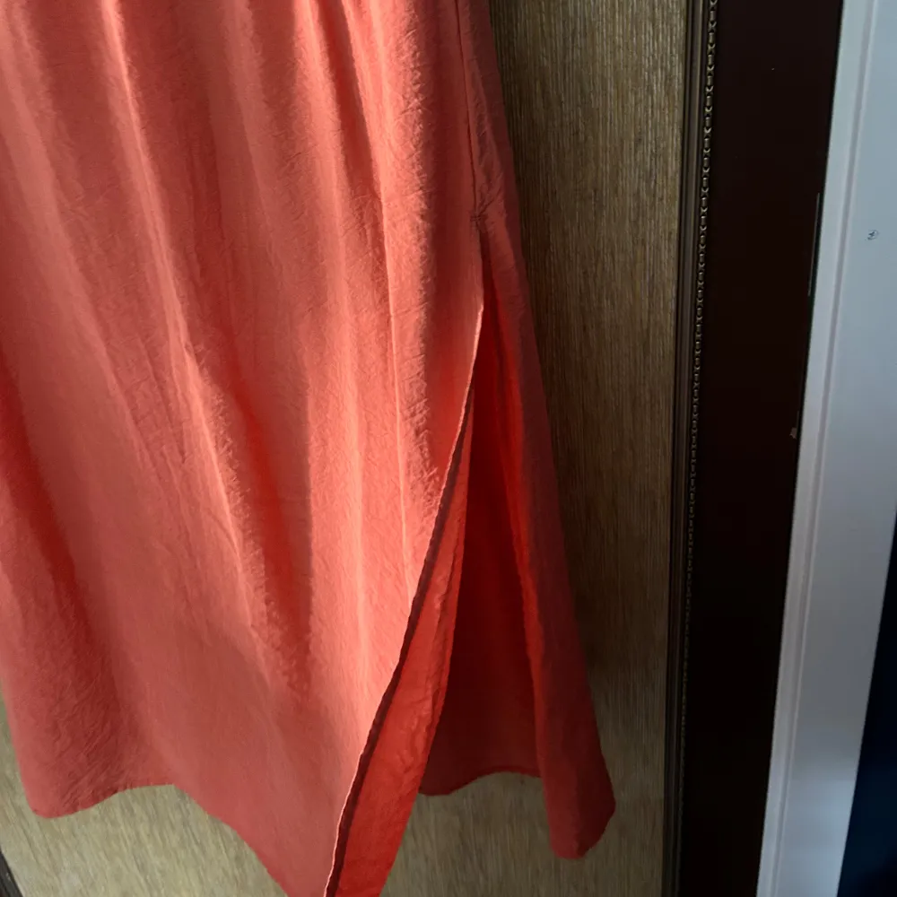 Säljer en superfin orange långkjol. Den är enkel och stilren med en elastisk midja som gör den bekväm att bära. Perfekt för sommaren eller våren! Kjolen är i ett lätt och luftigt material, vilket gör den idealisk för varma dagar. Passar både till vardags och fest. Den har slitsar på båda sidorna och fickor. . Hameet.