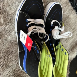 Svarta Vans sneakers med limegrön insida - Säljer ett par snygga Vans sneakers i svart med en cool limegrön insida. Skorna har vita snören och blå detaljer som ger dem en unik look. Perfekta för både vardag och fest!