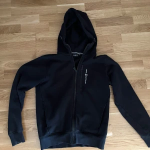 Svart hoodie från Sail racing - Säljer en svart Sail Racing hoodie i nästintill nyskick då jag knappt använt den. inga slitningar i materialet. Nypris 1500kr. Priset kan diskuteras.