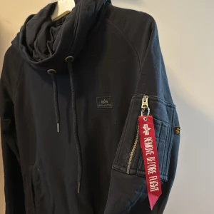 Hoodie från Alpha Industries dam - Svart hoodie från Alpha Industries. Fint skick. Storlek XS, passar nog också S. Hoodien har 2 fickor framme och 1 på vänster arm. Stor luva. 