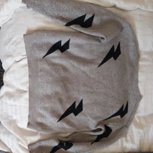 Grå stickad tröja med svarta blixtar - Säljer en supercool grå stickad tröja med svarta blixtar på. Den är i storlek s.. Perfekt för höst och vinter när man vill vara både varm och snygg. Tröjan är lite nopprig där av priset och väldigt bekväm att ha på sig. Passar perfekt till både jeans och kjol! (priset går att diskutera)