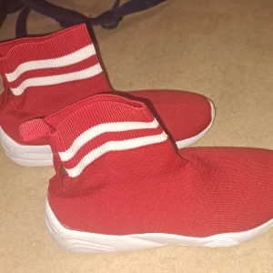Röda sneakers med vit sula - Säljer ett par snygga röda sneakers med vit sula. De har en stickad design med vita ränder runt ankeln. Perfekta för en sportig look och superbekväma att ha på sig. Passar bra till både vardag och träning. använd 1 gång bara.