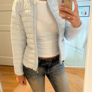 Ljusblå quiltad jacka - Säljer en superfin ljusblå quiltad jacka. Den är perfekt för vår och höst med sin lätta och bekväma passform. Jackan har en dragkedja framtill och två fickor med dragkedjor. Den är långärmad och har en stilren look som passar till det mesta. Perfekt för dig som vill ha en snygg och praktisk jacka!