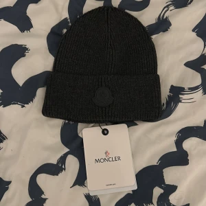 Moncler mössa  - Säljer en snygg grå/svart mössa från Moncler. Den är i nytt skick och Perfekt för att hålla sig varm speciellt nu under vintern. I färgen grå. Kostar 2900 på internet. Pris kan diskuteras 