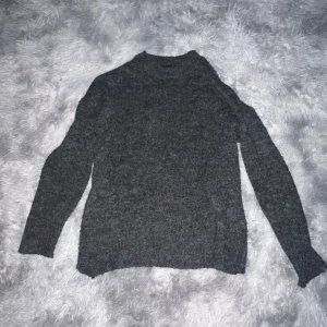 Mörkgrå stickad tröja - Säljer en mysig mörkgrå stickad tröja perfekt för kyliga dagar. Tröjan har en klassisk design med långa ärmar och en bekväm passform. Perfekt för både vardag och avslappnade tillfällen.