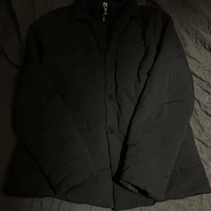 Svart kappa med dragkedja - Säljer en stilren svart kappa med dragkedja och knappar. Perfekt för höst och vinter. Den har långa ärmar och en klassisk design som passar till allt. Jackan är i bra skick och redo för nya äventyr. Passar både till vardags och fest!