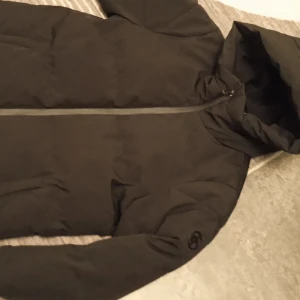 Cross sportswear vinterjacka  - Säljer en svart dunjacka i mycket bra skick. Den har en praktisk huva och dragkedja framtill. Perfekt för kalla vinterdagar. Jackan är långärmad och har en stilren design.