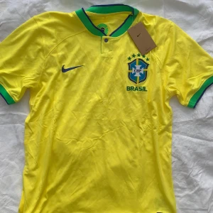 Gul Brasilien fotbollströja från Nike - KVITTO FINNS♥️Säljer en gul Brasilien fotbollströja från Nike i Dri-FIT material. Tröjan har korta ärmar och gröna detaljer vid kragen och ärmsluten. Perfekt för fotbollsfans som vill visa sitt stöd för Brasilien! 🟡🟢Storlek M Splitter Ny med taggar kvar 