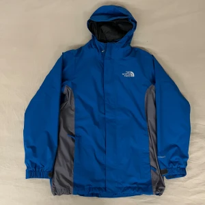 Blå vindjacka från The North Face - Säljer en blå vindjacka från The North Face i mycket bra skick. Jackan har en justerbar huva och dragkedja framtill. Perfekt för höst och vår, med ett stilrent utseende och praktiska fickor. Kan även användas på vintern då den jag en inbyggd fleece som går att ta av och på jackan som visat i bilderna.