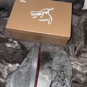 Grå sneakers från Christian Louboutin - Säljer ett par snygga grå sneakers från Christian Louboutin i mocka. De har den ikoniska röda sulan och snörning framtill. Skorna är i mycket bra skick och kommer med originalkartong. Perfekta för både vardag och fest!