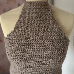 Beige virkad halterneck topp - Snygg beige virkad halterneck topp som är perfekt för både sommar och vår. Den har en tight passform och ärmlös design, vilket gör den idealisk för varmare dagar. Toppen är handgjord med ett grovt virkat mönster som ger en unik och trendig look.