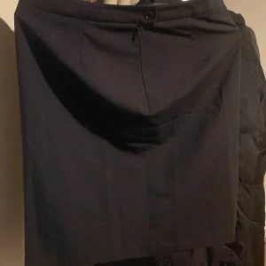 Svart kjol från SIR - Snygg svart kjol från SIR i klassisk stil. Kjolen har en knapp och dragkedja framtill för enkel påklädning. Perfekt för både vardag och festliga tillfällen. Den är i mycket bra skick och passar till alla säsonger. Ett måste i garderoben för en stilren look!
