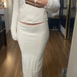 Vit stickad gina långkjol med slits - Säljer en superfin vit långkjol i stickat material. Kjolen har en elegant slits på sidan som ger en snygg detalj och gör den perfekt för både vardag och fest. Den är i bra skick och passar perfekt till höst- och vintergarderoben. Perfekt för dig som vill ha en stilren och bekväm look! 💫 Krämvit / vit färg. 🧸