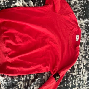 Röd sweatshirt från Stone Island - Säljer en snygg röd sweatshirt från Stone Island. Den har en klassisk rund hals och långa ärmar med den ikoniska loggan på ärmen. Perfekt för både vardag och chill. Passar bra till jeans eller joggers. Skön och stilren design! Pris kan diskuteras, väldigt bra skick!