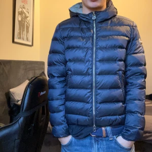 Mörkblå dunjacka från Colmar - Säljer en snygg mörkblå dunjacka från Colmar. Jackan har en dragkedja framtill och en mysig huva. Perfekt för kyliga dagar och håller dig varm och stilren. Den är i mycket bra skick och passar perfekt till både vardag och lite finare tillfällen.