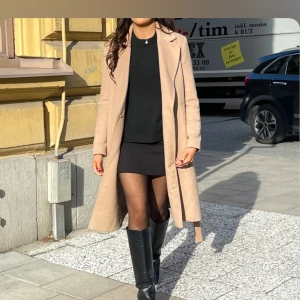 Beige kappa med knytband - Säljer en stilren beige kappa i mycket bra skick. Den har ett knytband i midjan för en snygg passform och långa ärmar. Äkta ull! Perfekt för höst och vår, och funkar både till vardags och fest. Kappan är i storlek dam m och ger en elegant look.