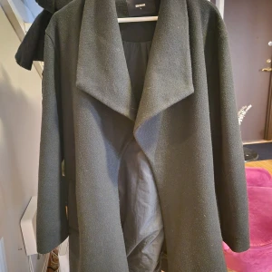 Svart kappa med bälte - Säljer en stilren svart kappa i bra skick. Den har långa ärmar och ett bälte i midjan för en snygg passform. Perfekt för höst och vinter, och funkar både till vardags och fest. Kappan har synliga tecken på användning. För flera bilder, skicka meddelande. Priset kan diskuteras.