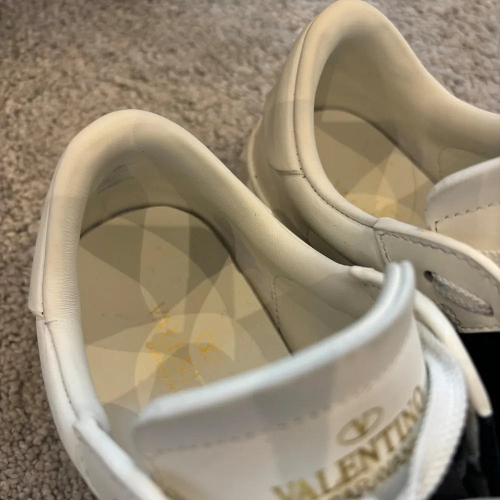 Säljer ett par snygga Valentino Garavani sneakers i vitt med en svart detalj över sidan. Jag köpte skorna här på Plick men de är en liten 39 (mer som 38,5) så de passade inte utifrån att jag är mer 39/40. Skorna har en cool design med nitar runt hälen och är i mycket bra skick. Perfekta för både vardag och fest! Obs! Står 39 i skon men jag väljer att lägga in den som 38,5 eftersom det mer överenstämmer storleken. Skor.