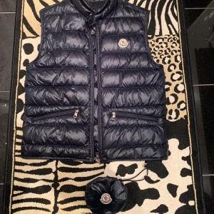 Moncler gui väst - Säljer denna Moncler gui västen då den har blivit för liten för mig. 9/10 skick använd ett fåtal gånger. Mörkblå och storlek 1 vilket motsvarar S/XS Man får med påsen och alla extra grejer. Hör av er om det är något speciellt. Kan tänkas gå ner i pris vid snabb affär!