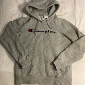 Grå hoodie från Champion - Säljer en grå hoodie från Champion i bra skick. Den har en klassisk design med Champion-loggan på bröstet och en mysig insida. Har nästan osynlig fläck med smink på sidan av huddi luvan men som inte syns med Huddin på