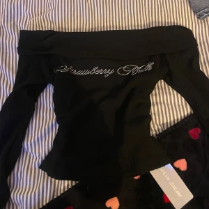 Svart offshoulder topp  - Snygg svart offshoulder topp från Shein med texten 'Strawberry Milk' i glittriga bokstäver. Toppen är i ett ribbat material och har en tight passform som framhäver figuren❣️Den är aldrig använd och har lappen kvar❣️Säljer för att den inte kommer till användning❣️