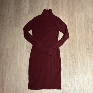Vinröd stickad klänning - Säljer en mysig vinröd stickad klänning med polokrage. Den är långärmad och har en tight passform som passar perfekt för höst och vinter. Klänningen är i mycket bra skick och är superbekväm att ha på sig. Perfekt för både vardag och festliga tillfällen!