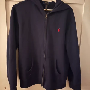 Mörkblå hoodie från Polo Ralph Lauren - Säljer en snygg mörkblå hoodie från Polo Ralph Lauren i storlek XL. Den har en dragkedja framtill och den klassiska röda loggan på bröstet. Den är använd Max 5 gånger, i väldigt bra skick. || Nypris 1 200kr men priset kan diskuteras 