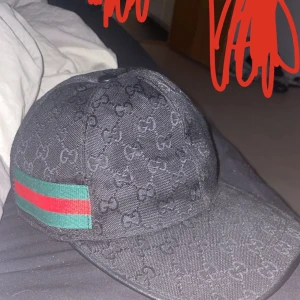 SVART GUCCI KEPS - Snygg svart keps med diskret mönster och en grön och röd randdetalj på sidan. Perfekt för att ge din outfit en cool touch. Passar bra till både vardag och fest! Är använd få tal gånger box följer med pris kan diskuteras vid snabb affär