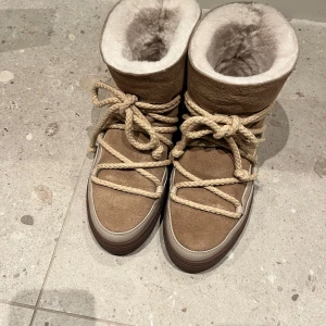 Beige vinterstövlar från Inuikii - Säljer ett par snygga och varma beige vinterskor från Inuikii. De är i mocka med en mysig pälsfodring och har rejäla snören för en cool look. Perfekta för kalla vinterdagar, och det är helt nya är använda max två gånger.❄️