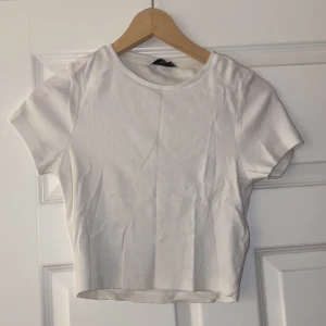 Vit ribbad crop-top från Pigalle - Säljer en enkel och stilren vit ribbad crop-top från Pigalle i storlek M. Den har en klassisk rund hals och korta ärmar, perfekt för vardagsbruk eller att styla upp med accessoarer. Toppen har aldrig använts och passar till alla säsonger.