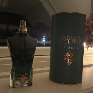 Jean Paul Gaultier Le Beau Le Parfum - Säljer en elegant parfymflaska från Jean Paul Gaultier, Le Beau Le Parfum. Flaskan har en unik design i form av en manlig torso i mörkblått glas med gulddetaljer. Den kommer med en matchande cylindrisk förpackning. Perfekt för den som vill ha en lyxig och stilren doftupplevelse.
