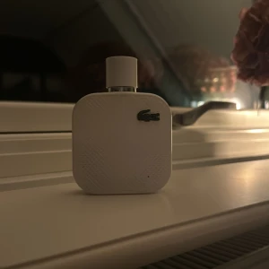 Vit parfymflaska från Lacoste - Säljer en stilren vit parfymflaska från Lacoste. Flaskan har en fyrkantig form med rundade hörn och pryds av den klassiska Lacoste-loggan i metall. Perfekt för den som gillar en fräsch och sportig doft. Passar både till vardags och fest!