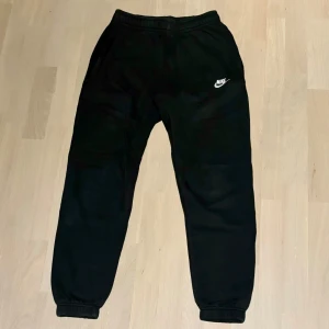 Svarta mjukisbyxor från Nike - Säljer ett par svarta mjukisbyxor från Nike i storlek XS. De är i bra skick och passar perfekta för träning eller bara chill i vardagen. Byxorna har en klassisk design med Nike-loggan på sidan och har inte defekter. Nypris: 699kr 