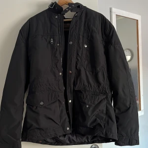 Svart jacka från Zara Man - Säljer en svart jacka från Zara Man med dragkedja och knappar. Jackan har flera praktiska fickor och en quiltad design på baksidan. Perfekt för höst och vinter.