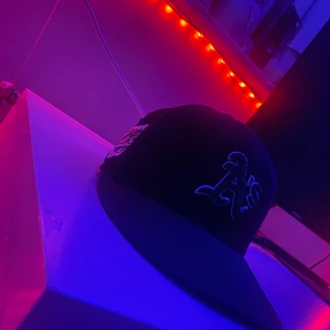 Svart grön keps från New Era - Snygg svart grön keps från New Era med broderad logga och World Series-märke. Perfekt för att ge din outfit en sportig touch. Kepsen har en klassisk passform och är tillverkad i bomull.