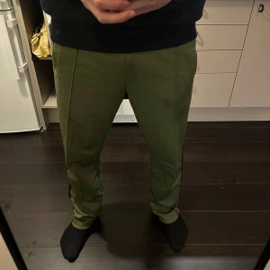 Palm angels byxor, strl L - Snygga gröna byxor med en lila rand längs sidan. Byxorna har en avslappnad passform och är perfekta för en casual look. De har elastisk midja för extra komfort. Jag är 185 och väger cirka 84 kg!